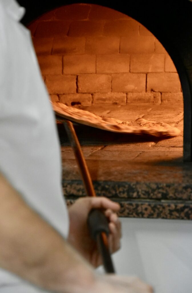 Il pizzaiolo inforna la pizza nel forno a legna