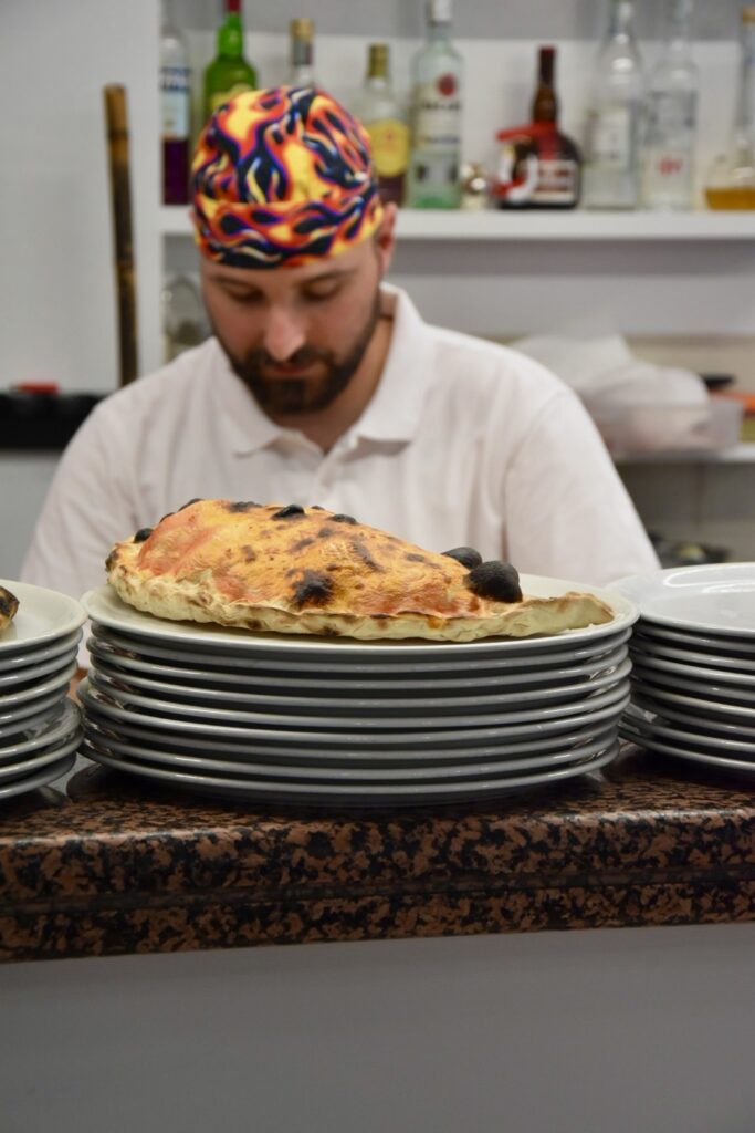 Calzone in primo piano con pizzaiolo che lavora sullo sfondo